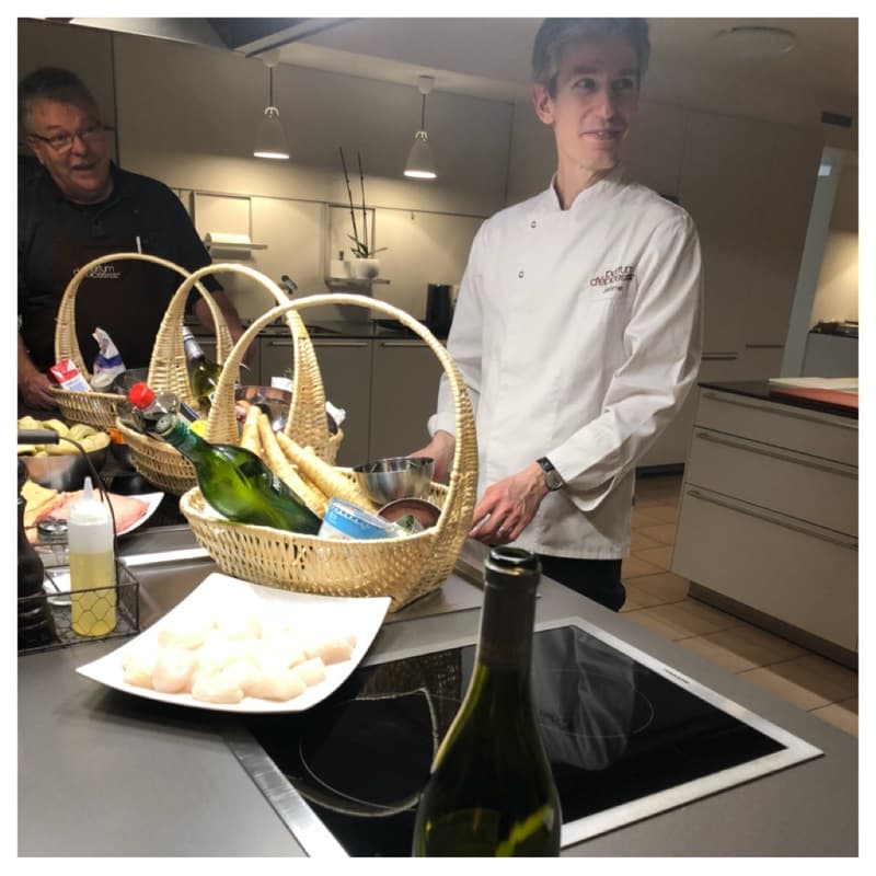 Chef Jérôme en veste blanche présentant un panier d'osier rempli d'ingrédients, en atelier culinaire aphrodisiaque chez Parfum d'Epices