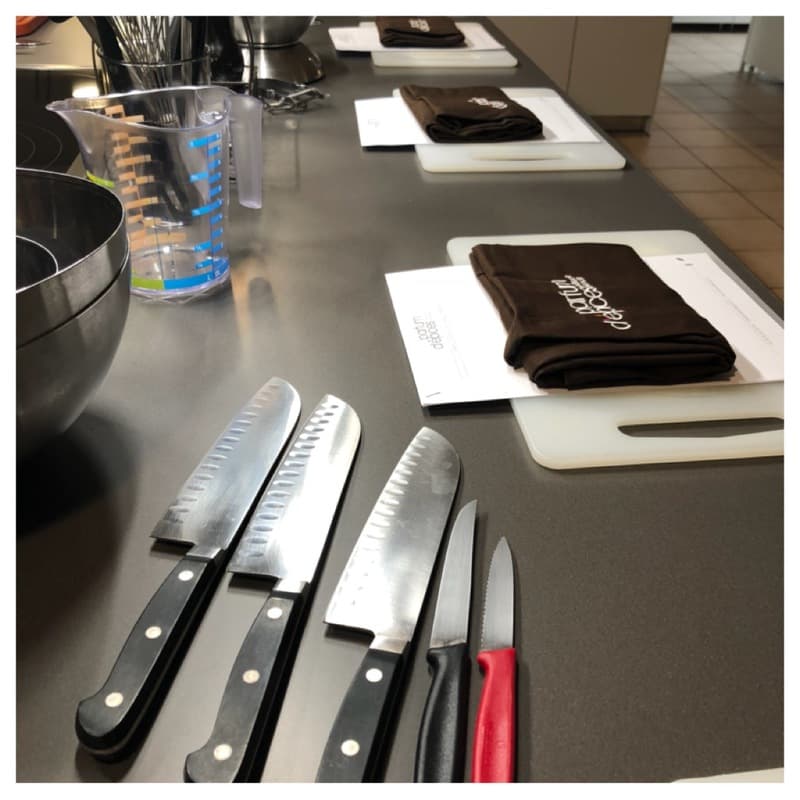 Couteaux de cuisine alignés sur un plan de travail gris avec serviettes noires et blanches, préparation d'un atelier culinaire