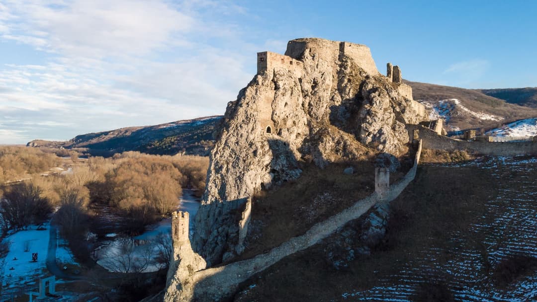 Ruines d'un château médiéval perché sur un rocher escarpé en Europe centrale, vallée enneigée et rivière en contrebas