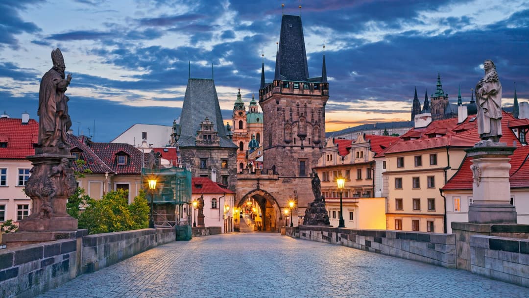 Pont de pierre avec statues, tours gothiques et toits rouges illuminés au crépuscule à Prague