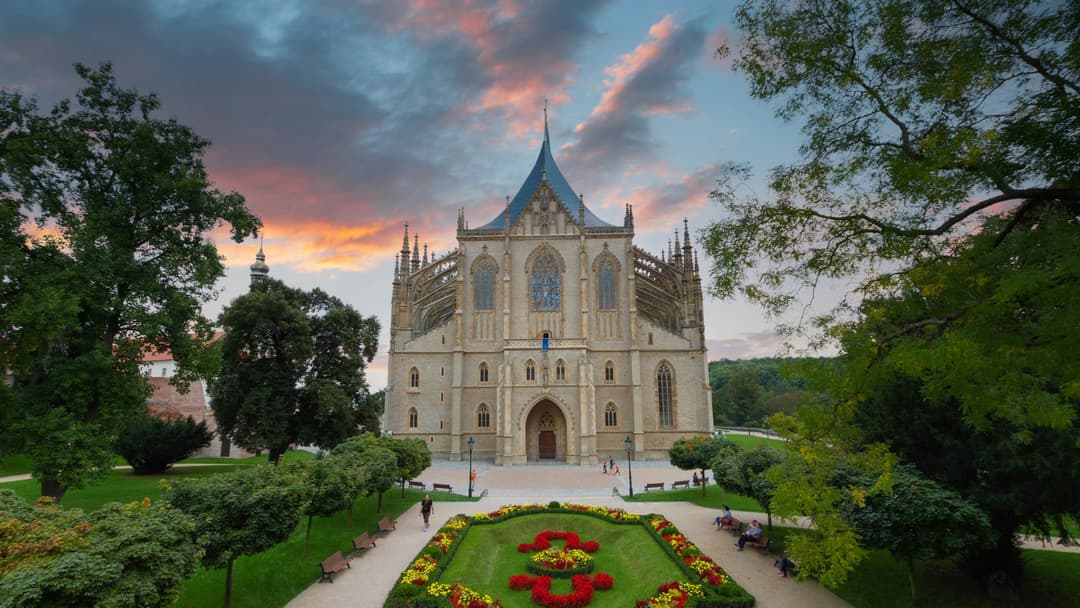 Cathédrale gothique blanche de Hongrie avec tours pointues, entourée d'arbres verts et d'un jardin fleuri au coucher du soleil