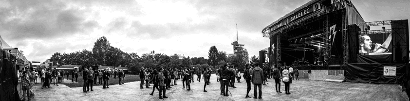 Scène principale du festival Balélec avec foule de visiteurs dispersés sur le site en noir et blanc
