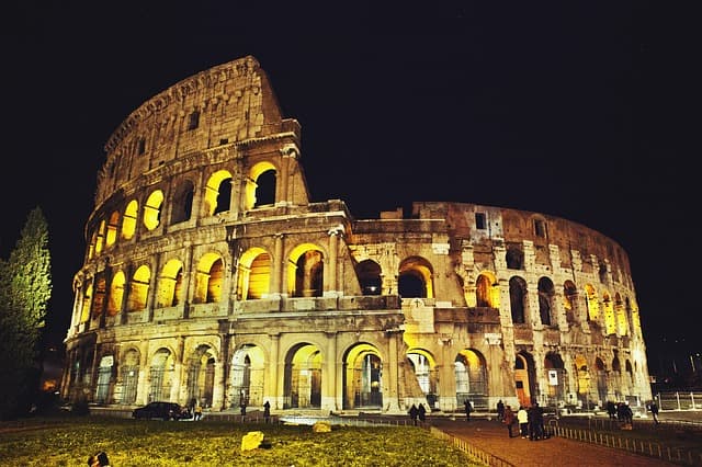 Le Colisée de Rome illuminé la nuit, ses arcades dorées détachées sur le ciel noir, avec des visiteurs au pied du monument antique