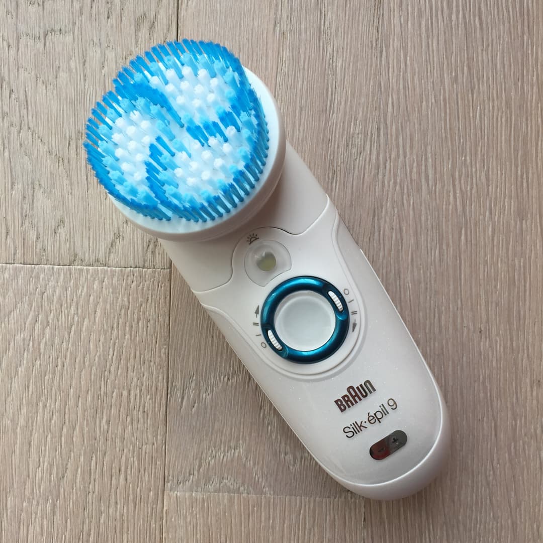 Épilateur Braun Silk Epil 9 blanc et bleu avec tête large et accessoire de nettoyage facial, sur fond de bois gris