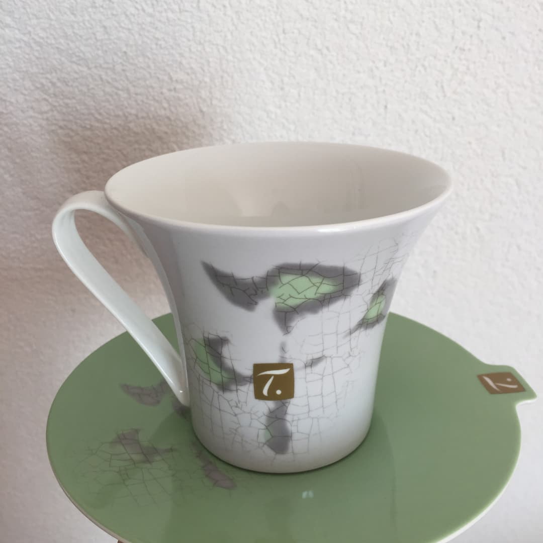 Tasse SPECIAL.T blanche décorée de feuilles de thé, posée sur une soucoupe verte