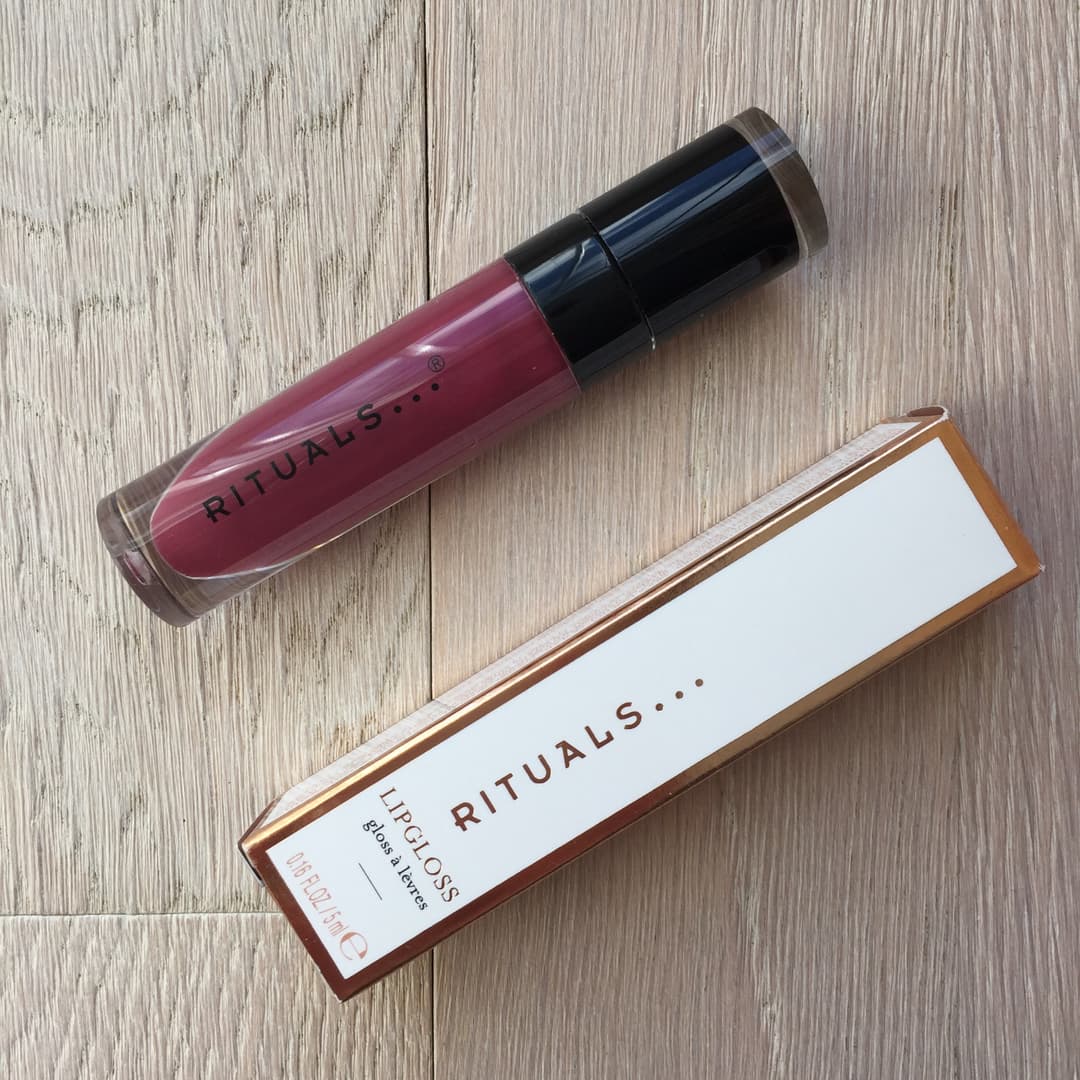 Rituals lipgloss de couleur prune-violet sheer avec son emballage de teinte beige et dorée sur bois clair