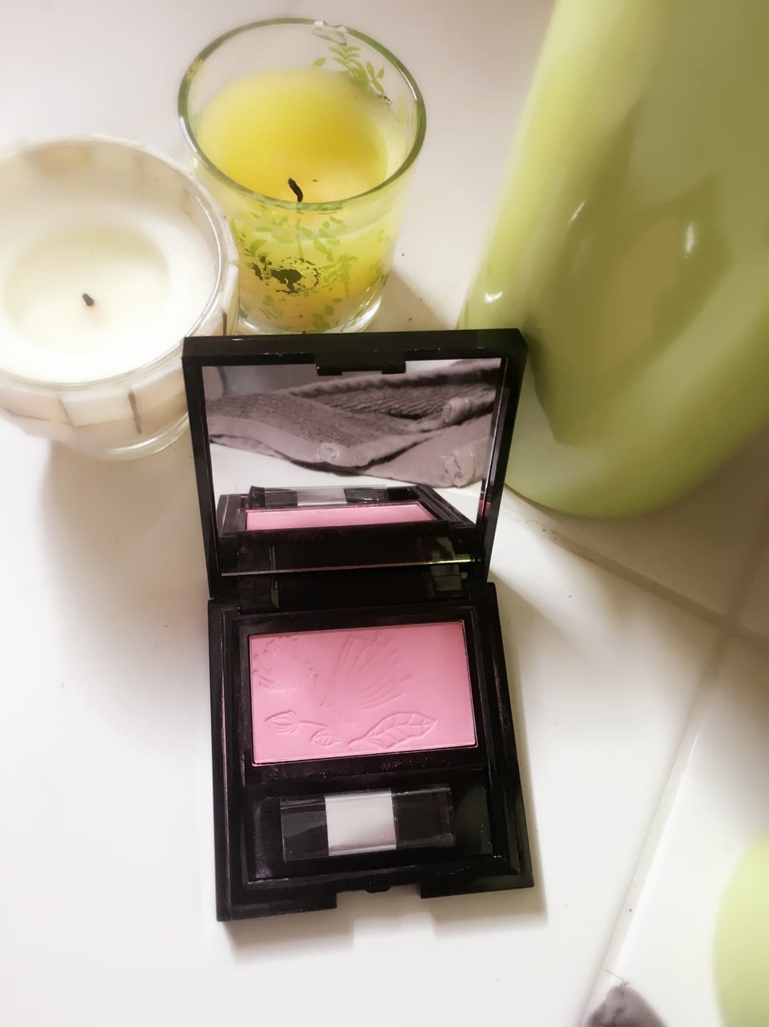 Rituals Magic Powder Blush en boîte noire ouverte affichant sa poudre rose clair, entourée d'une bougie et d'une infusion jaune