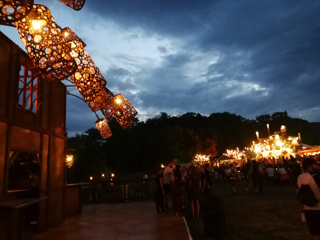 Scène du Paléo Festival de Nyon la nuit, avec lanternes dorées illuminées et foule de festivaliers sous un ciel bleu foncé