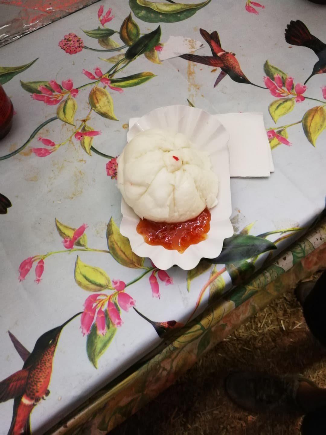 Rouleau de printemps vietnamien garni de sauce rouge sur assiette blanche, posée sur une nappe à motifs floraux roses et verts