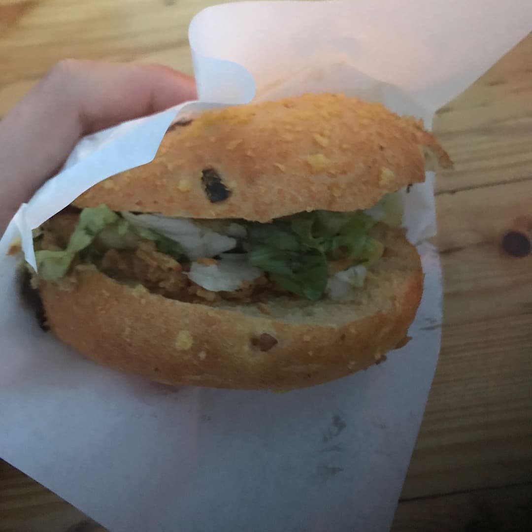 Burger mexicain tenu à la main, garni de laitue et d'oignons, dans un emballage blanc au Paléo Festival