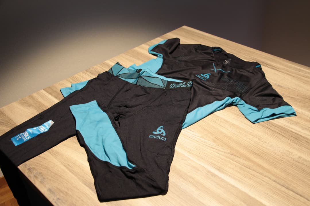 T-shirt et collant de course ODLO Ceramicool Pro noirs avec détails bleu ciel, posés sur une table en bois