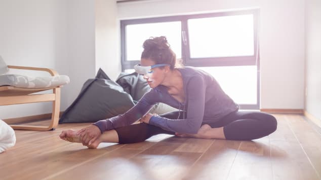 Femme portant des lunettes de luminothérapie lors d'une séance d'étirement au sol dans une pièce lumineuse