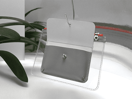 Wallet Barnett de Marlich en cuir gris et PVC transparent, avec porte-cartes intérieur et fermeture-éclair, présenté aux côtés d'une plante verte