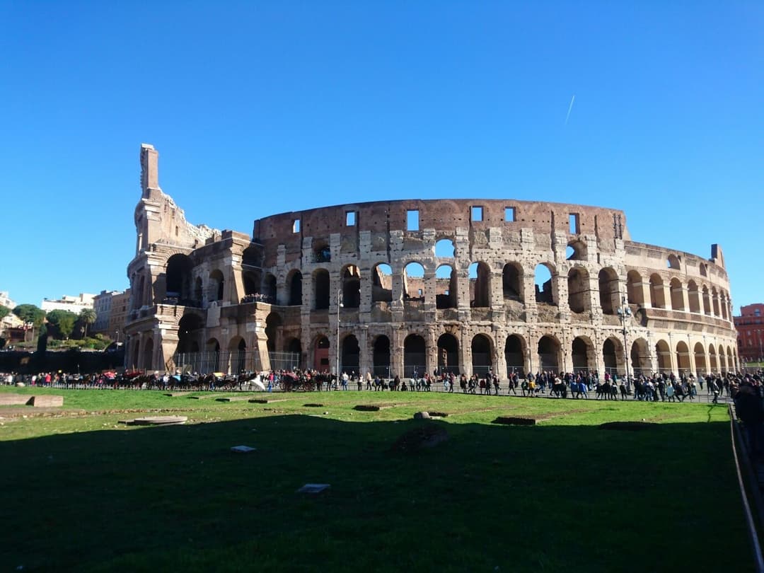Le Colosseum de Rome sous un ciel bleu dégagé, avec des visiteurs dispersés autour de ses ruines en pierre