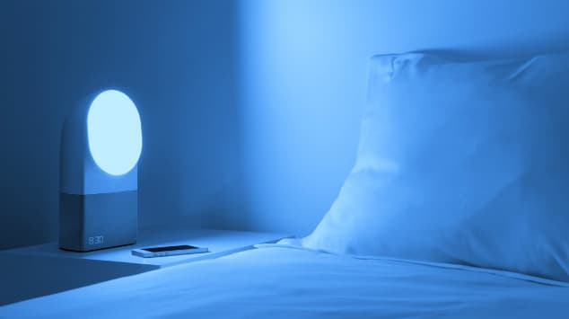 Lampe de luminothérapie Philips avec écran affichant l'heure, émettant une lumière bleue blanche sur un lit dans une chambre