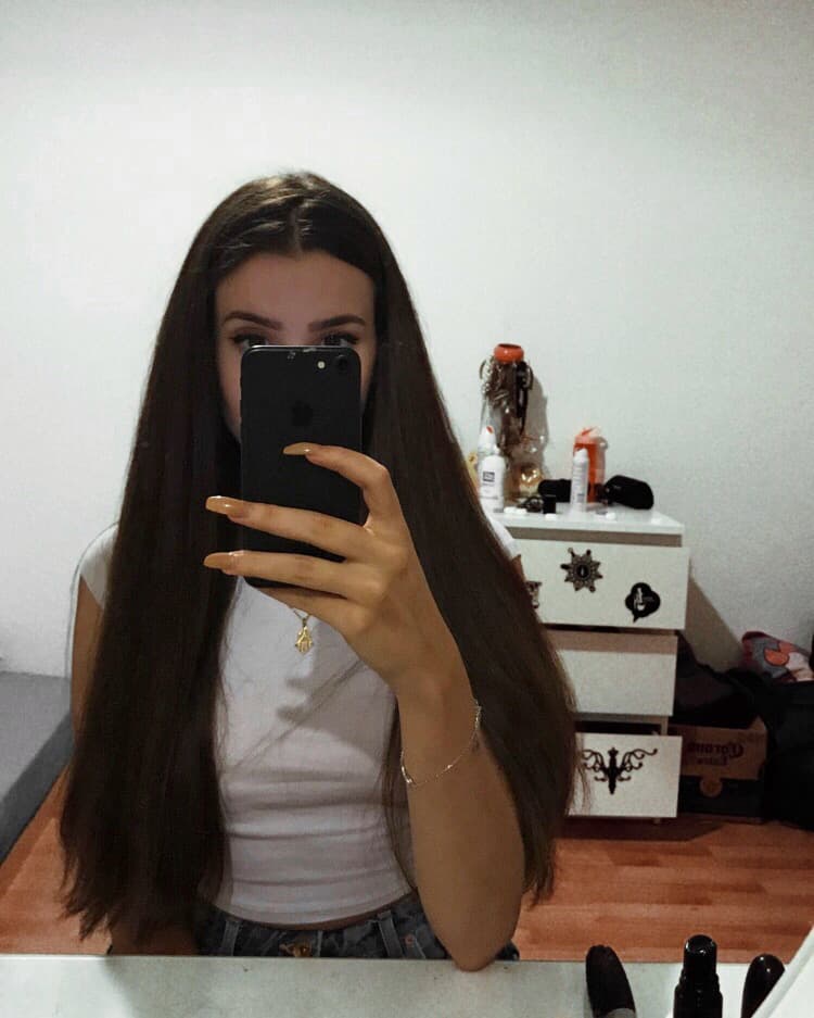 Femme aux longs cheveux bruns brillants se prenant en selfie devant ses produits de soins capillaires