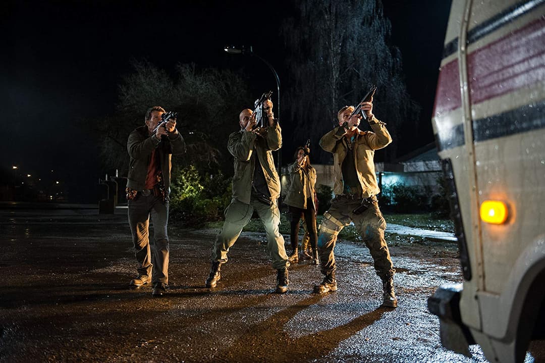 Groupe de soldats armés de fusils pointant leurs armes vers le ciel dans une cour la nuit, éclairés par des projecteurs