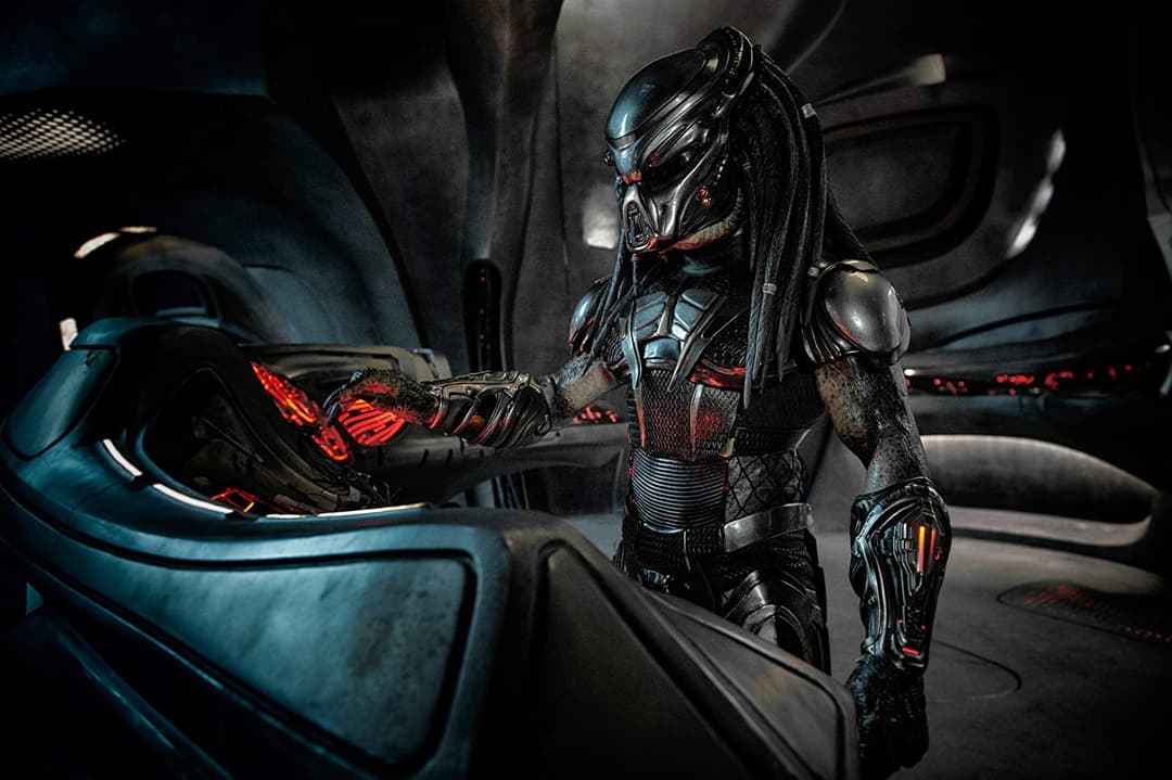 Un Predator en armure noire et métallisée, équipé d'une arme lumineuse rouge, dans l'habitacle d'un vaisseau futuriste