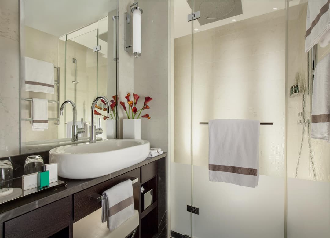 Salle de bains luxueuse avec lavabo blanc ovale, mobilier bois foncé, miroir large, fleurs rouges et paroi de douche vitrée