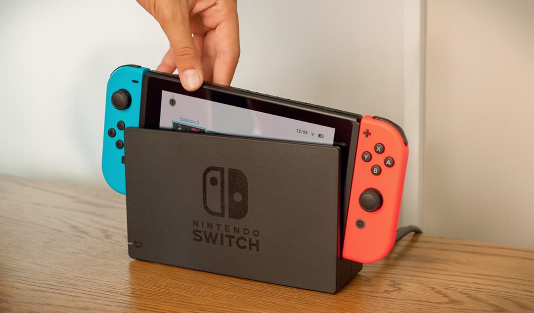 Nintendo Switch avec manettes Joy-Con bleu et rouge, tenue en main sur une table en bois