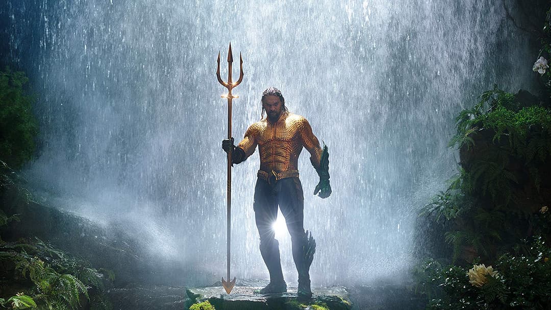 Aquaman en armure dorée tenant un trident sous une cascade, entouré de végétation luxuriante