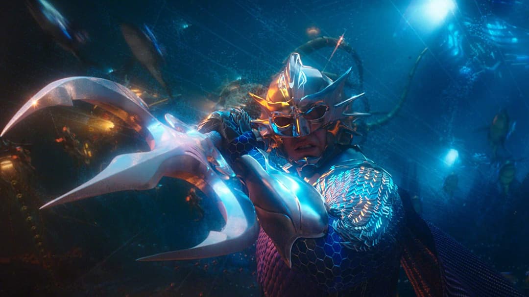 Aquaman en armure dorée et bleue brandit un trident luminescent sous l'eau dans une scène du film