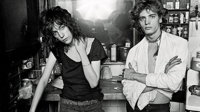 Noir et blanc de deux jeunes artistes dans un atelier, l'un en t-shirt noir et l'autre en chemise blanche, entourés de matériel créatif