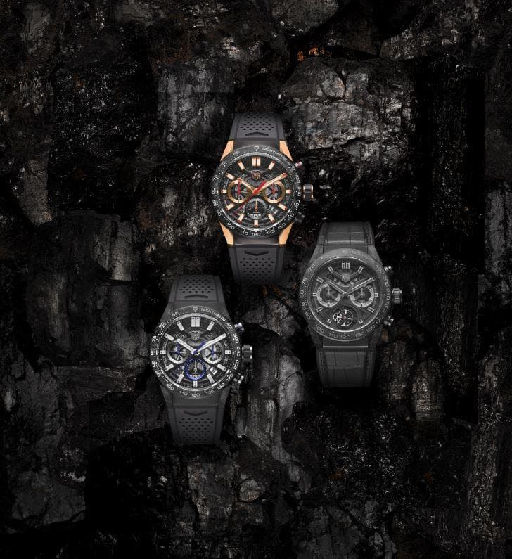 Trois montres TAG Heuer Carrera en carbone avec bracelets noirs, dont une avec accents dorés, posées sur une surface texturée grise et noire
