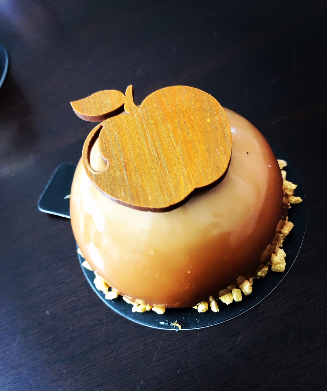 Le Golden, pâtisserie sphérique à glaçage doré avec feuille de caramel, mousse fleur de lait et compotée tatin, sur socle noir