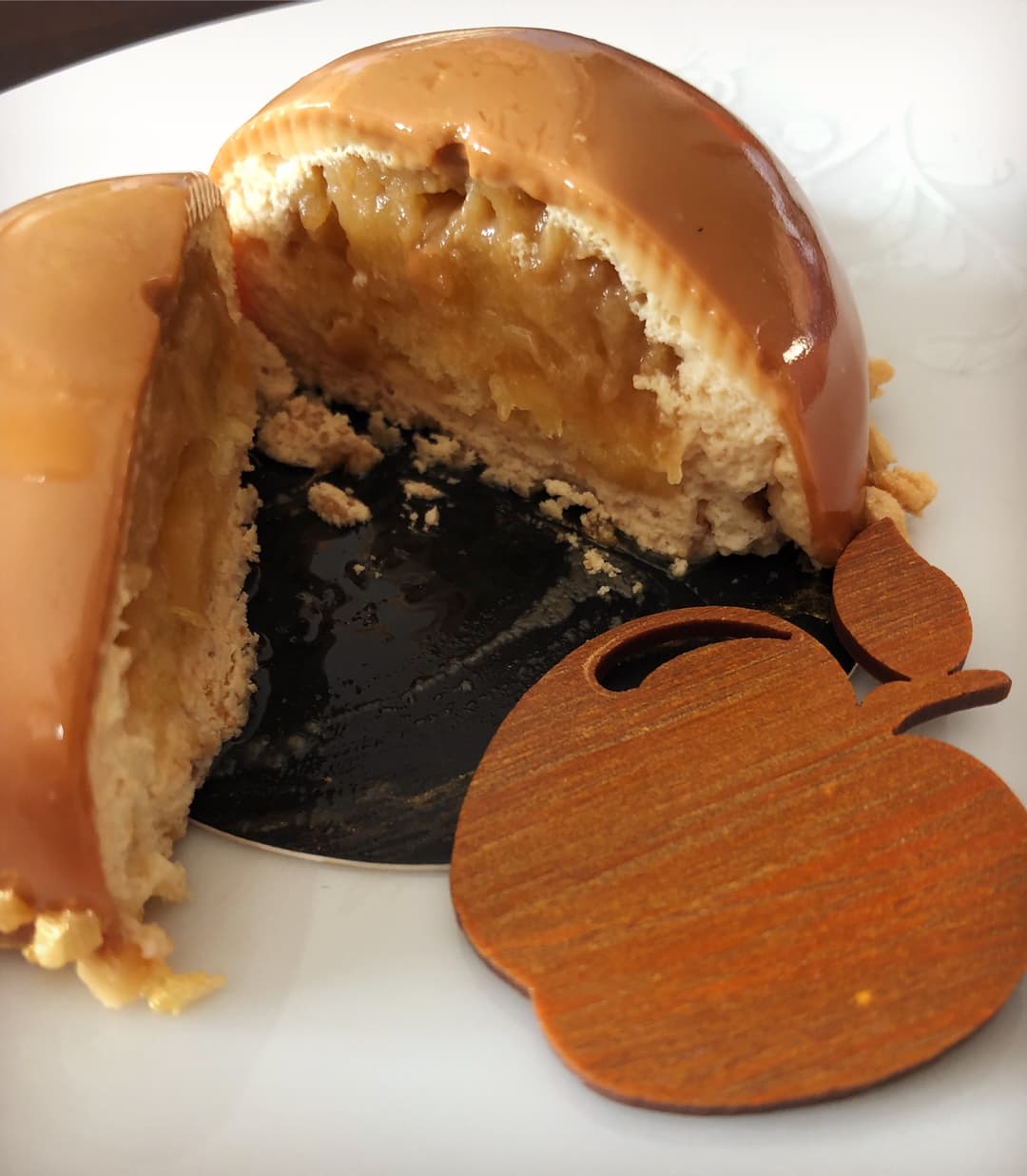 Pâtisserie Golden dorée coupée en deux, révélant une mousse fleur de lait et une compotée tatin noire, accompagnée d'une feuille en bois