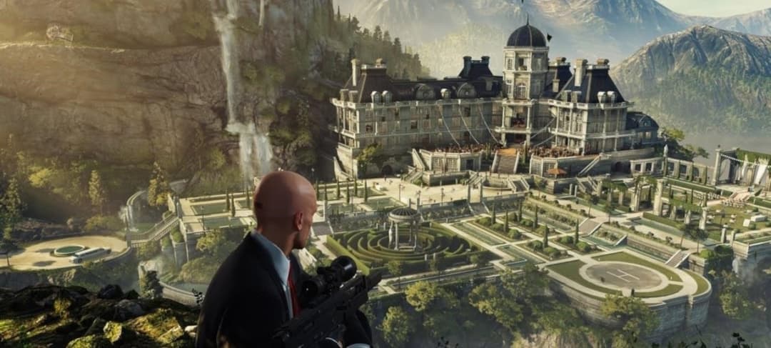 Agent 47 chauve en costume noir avec une arme, face à un grand château dans une vallée de montagne