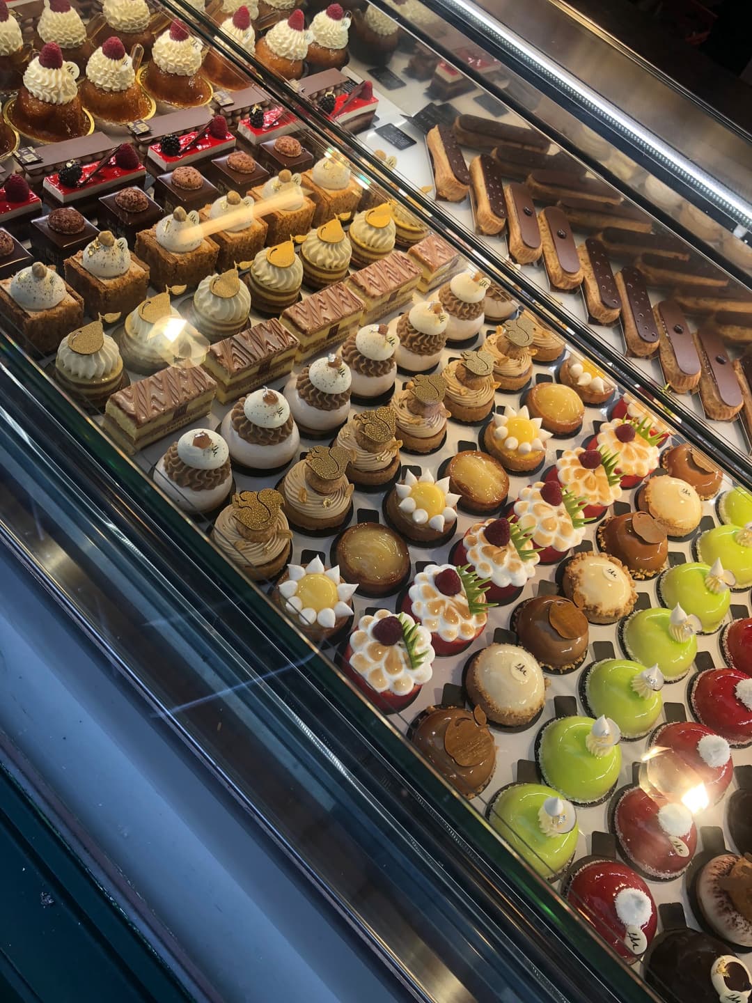 Vitrine réfrigérée de pâtisserie Moutarlier présentant diverses pâtisseries : tartelettes aux fruits rouges, éclairs, choux à la crème, gâteaux au chocolat et pièces montées