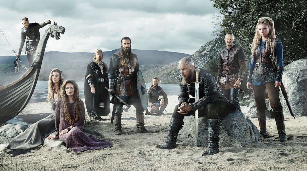 Ragnar Lodbrok et ses guerriers vikings sur une plage avec un drakkar, face à la mer et aux montagnes