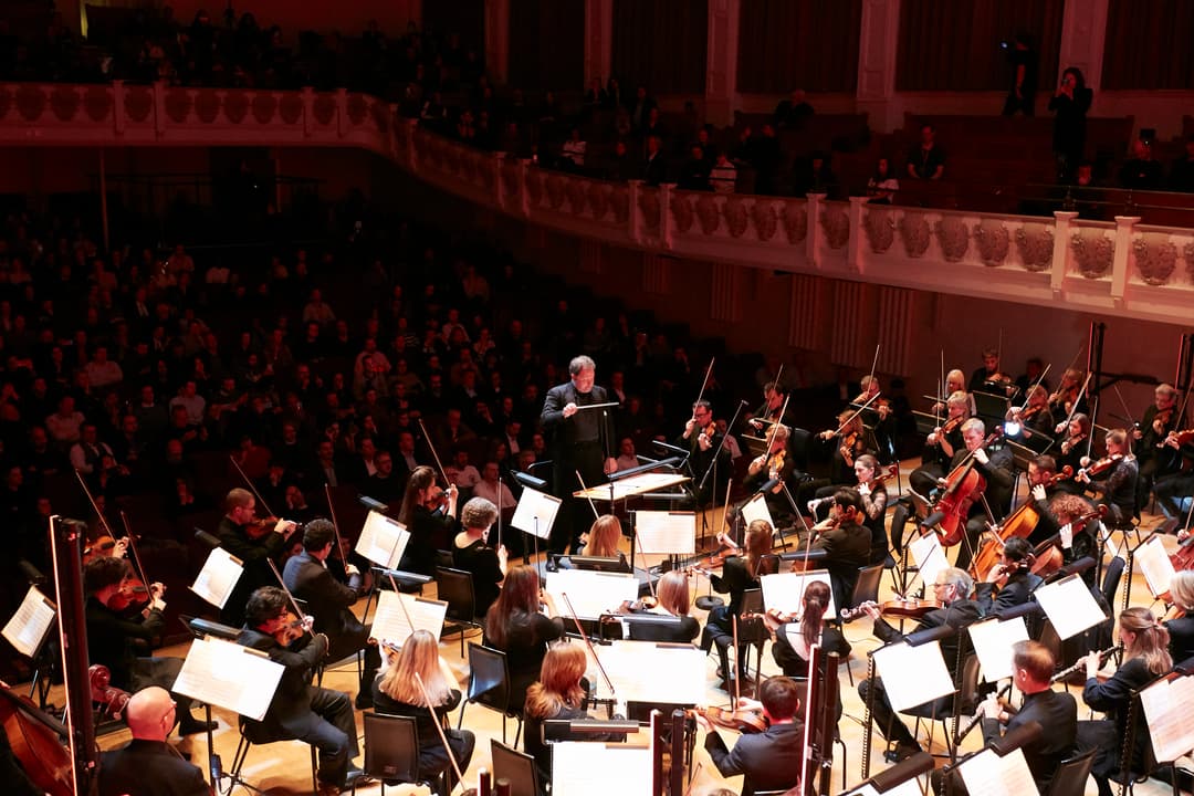 Orchestre symphonique complet en concert au Cadogan Hall de Londres, dirigé par un chef d'orchestre, illuminé par une lumière rouge-orangé chaud