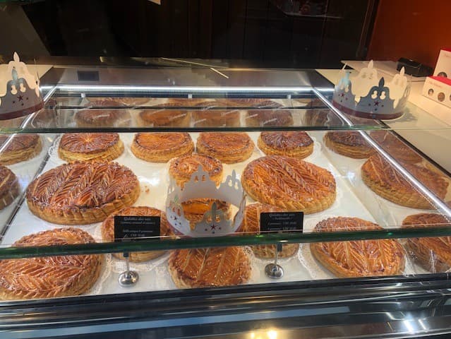 Vitrine de pâtisserie avec différents croissants et pains au chocolat disposés sur des plateaux blancs, éclairés par des lampes, en arrière-plan murs orange