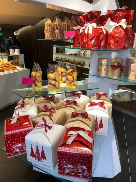 Vitrine du salon de thé Lucien Moutarlier avec pâtisseries, coffrets cadeaux rouges et blanc, et étalage de produits gourmands