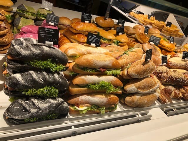 Vitrine de boulangerie présentant des sandwiches garnis et des pains artisanaux variés, dont des pains noirs, baguettes et pains complets