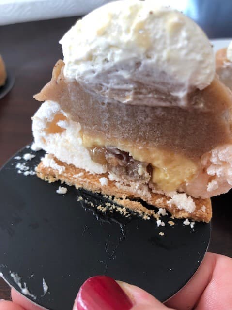 Pâtisserie Meringué marron garnie de chantilly vanille, sur biscuit sablé parsemé de sucre, présentée sur une ardoise noire