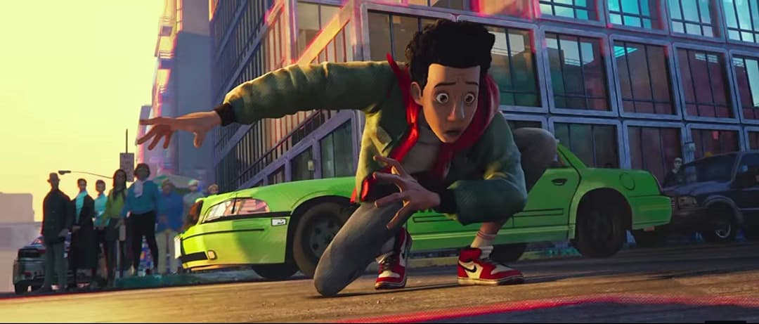 Miles Morales, jeune homme afro-américain en hoodie rouge et vert, en position de combat dans une rue de Brooklyn avec des voitures et des immeubles