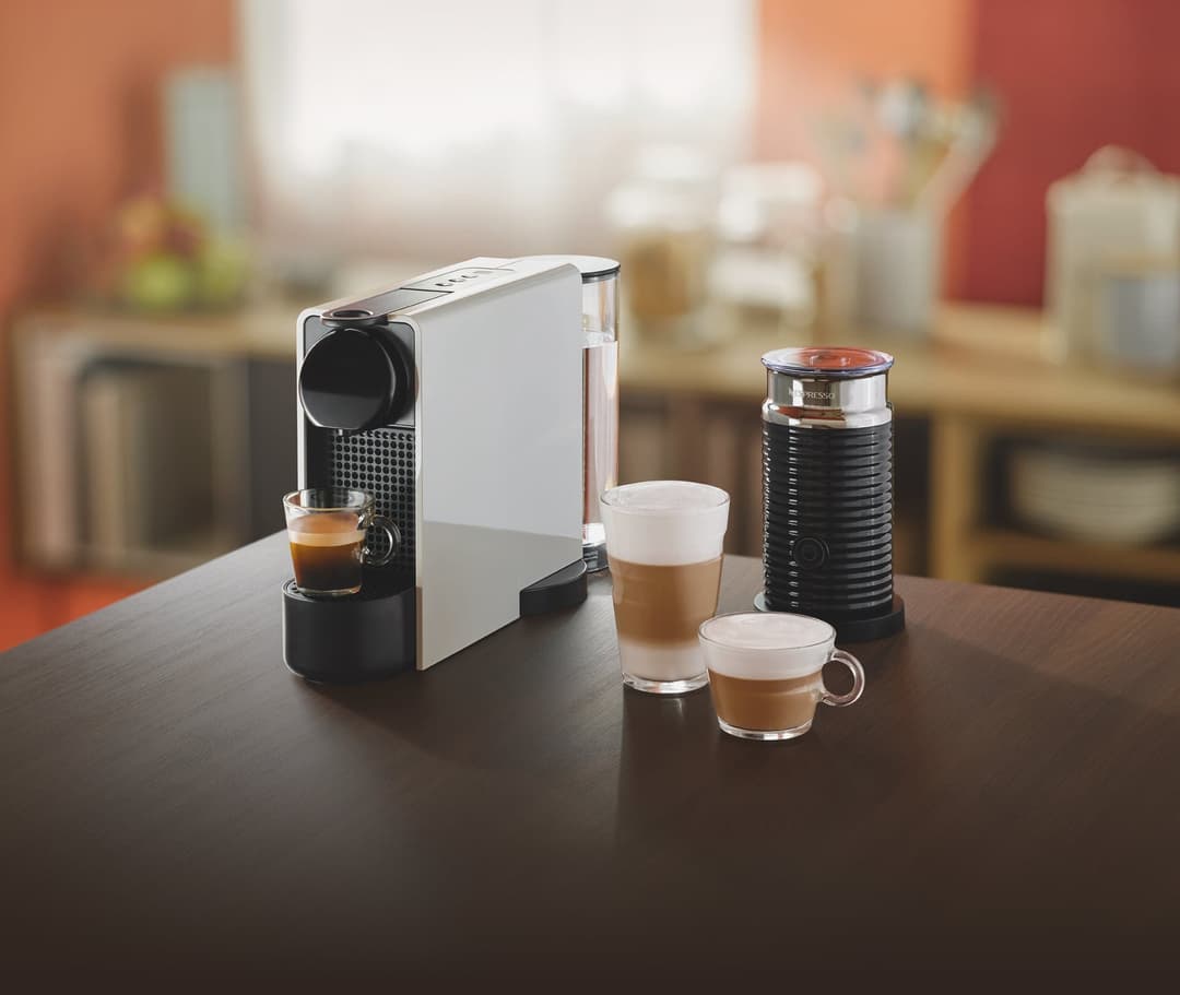 Machine Nespresso Essenza Plus blanche et noire avec mousseur de lait noir et tasses de café sur un plan de travail