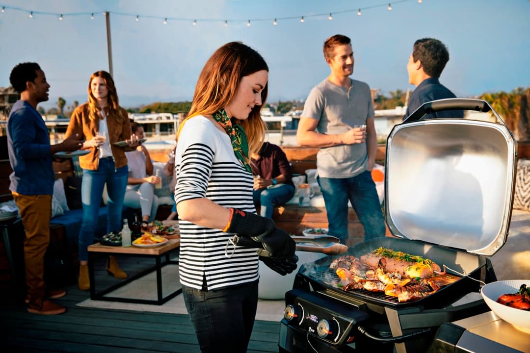 Femme en marinière grillant des brochettes sur un gril électrique Weber lors d'une réception en terrasse ensoleillée