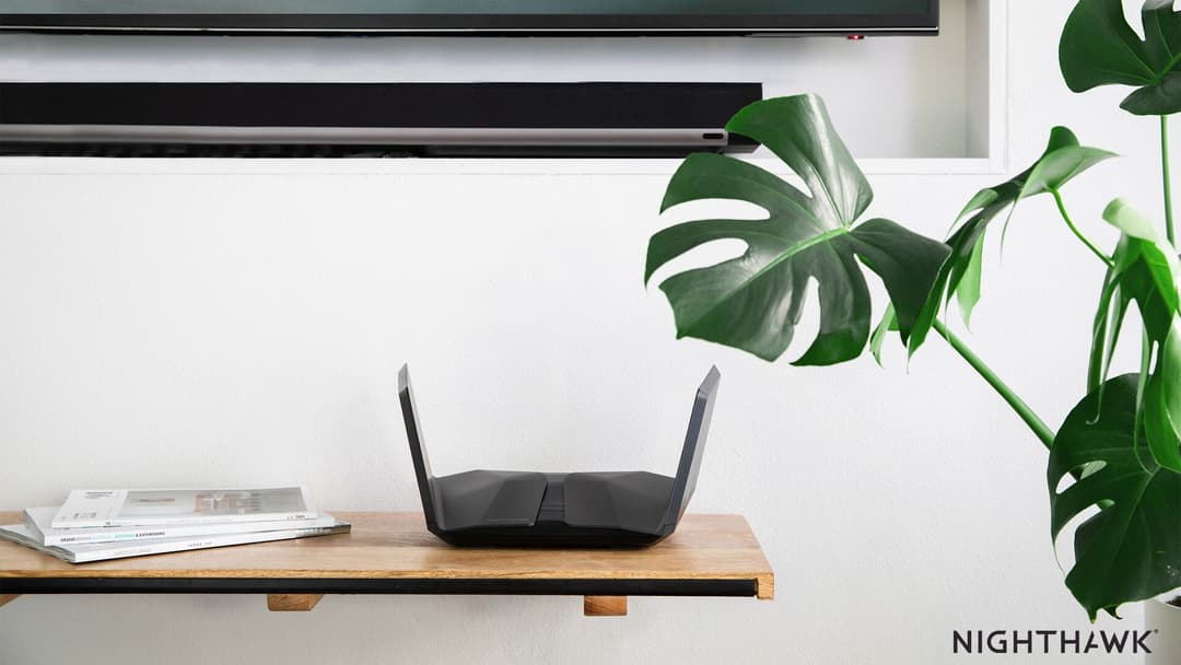 Routeur Netgear Nighthawk Wi-Fi 6 noir avec deux antennes, posé sur une table en bois près de plantes vertes