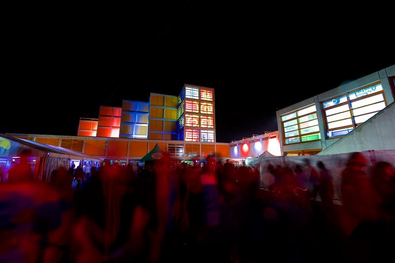 Foule de spectateurs devant une scène illuminée avec structures colorées à Baleinev, festival techno en soirée