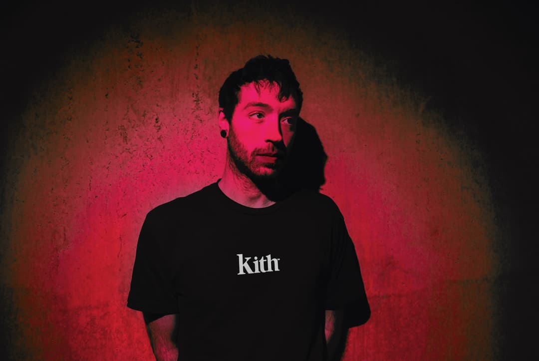 Producteur électronique Unders en t-shirt noir sur fond rouge, regardant vers la caméra