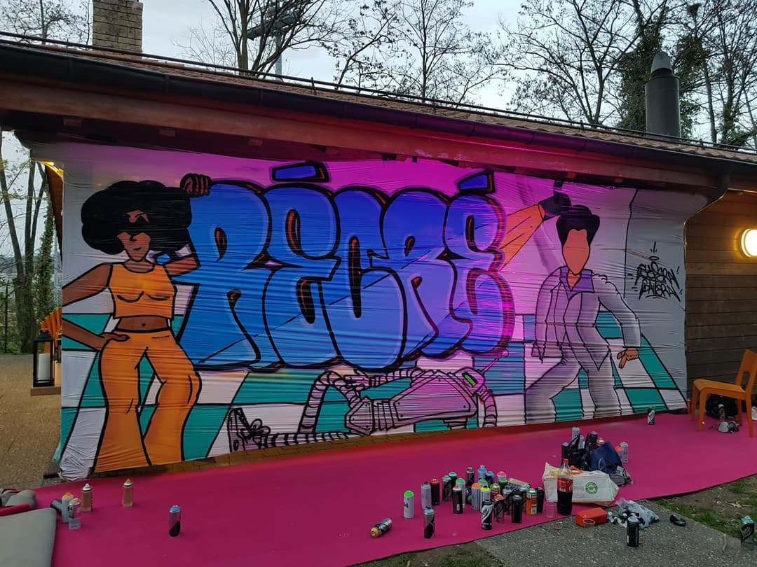 Fresque murale colorée avec personnages stylisés et graff bleu au Festival Balélec 2019, sol rose vif jonché de bombes de peinture