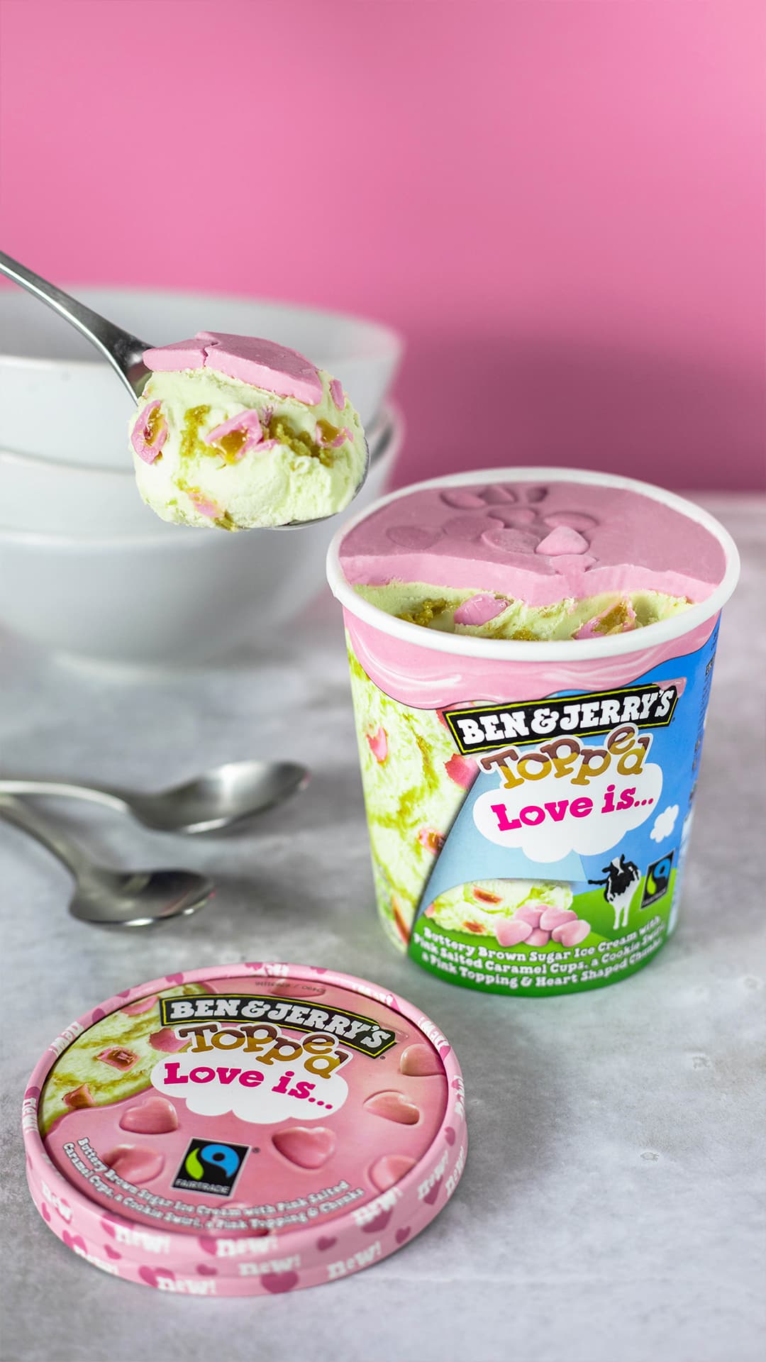 Gobelet de glace Ben & Jerry's Love is... au caramel beurre avec swirls cookie et chunks roses en cœur, cuillère de glace soulevée au-dessus