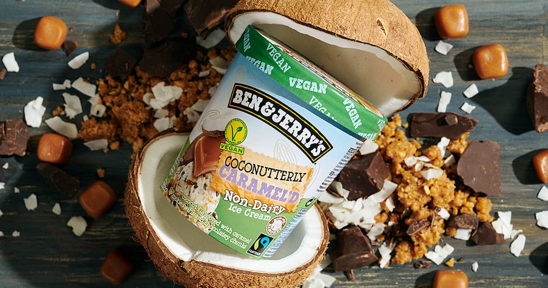 Pot de glace végane Ben & Jerry's Coconutterly Caramel'd présenté dans une demi-noix de coco, entouré de caramel, cookies et copeaux de chocolat