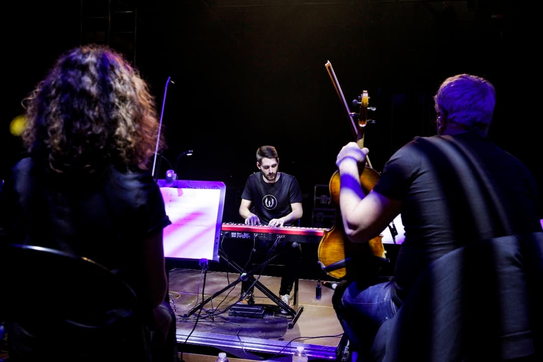 Worakls au clavier entouré de musiciens avec violoncelles et instruments à cordes sur scène, éclairage bleu et violet