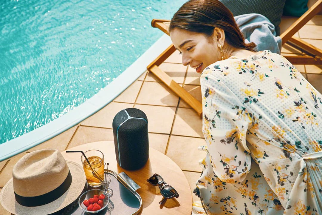 Enceinte Sony SRS-XB402M noire à côté d'une piscine, avec une femme souriante près d'accessoires d'été