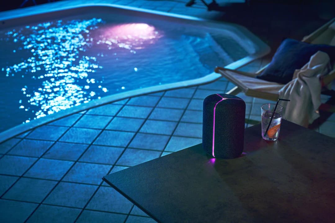 Enceinte Sony XB402M noire avec bande LED rose posée au bord d'une piscine, à côté d'un verre